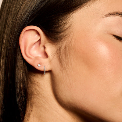 Oorring van 14k wit goud met glinsterende zirkonia aan oorlel  .