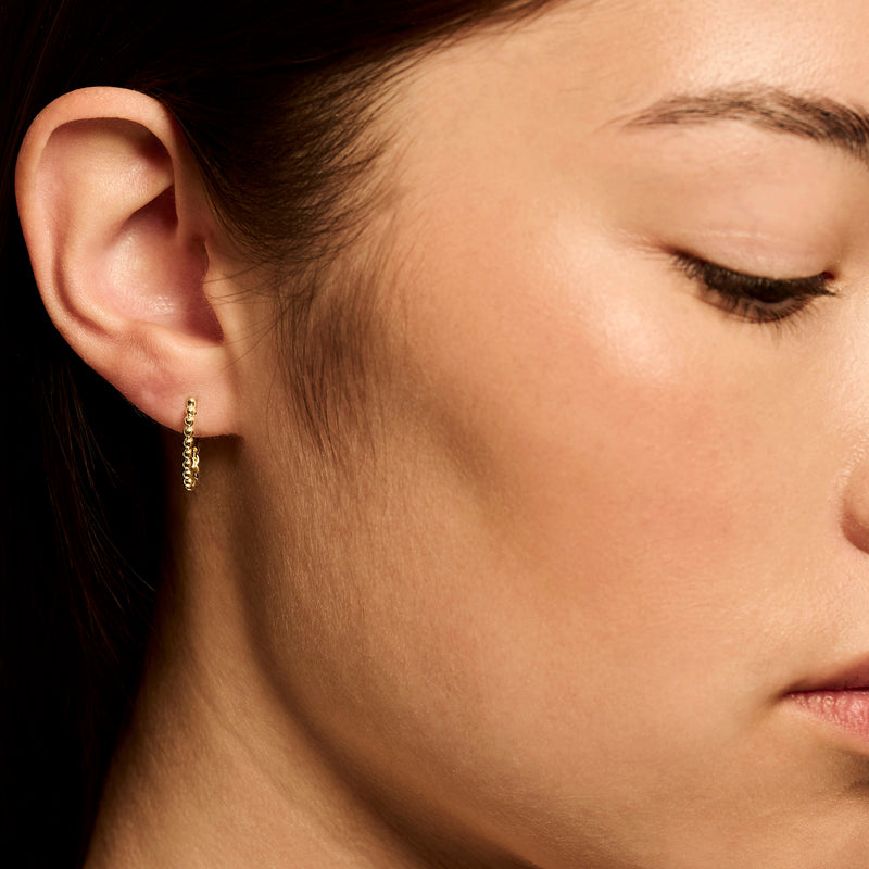 Anneaux d'oreilles en or jaune 14k avec des liens circulaires subtils sur l'oreille de la femme.