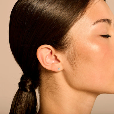 Witte diamanten oorknop van 14k wit goud gedragen in oor van vrouw met strakke paardenstaart.