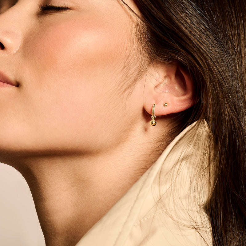 14k geelgouden oorbellen met kleine ronde hanger naast gouden studs.