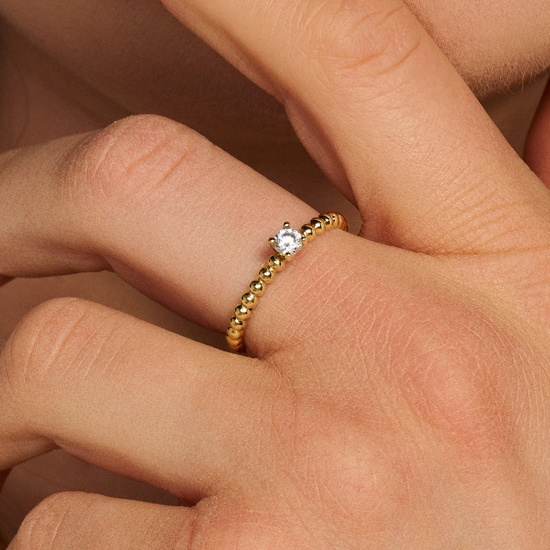 14k gouden ring met bolletjesmotief en solitair zirkonia op vinger.