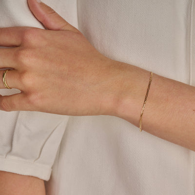 Fijne armband van 14k goud met schakelpatroon om pols bij lichte blouse.