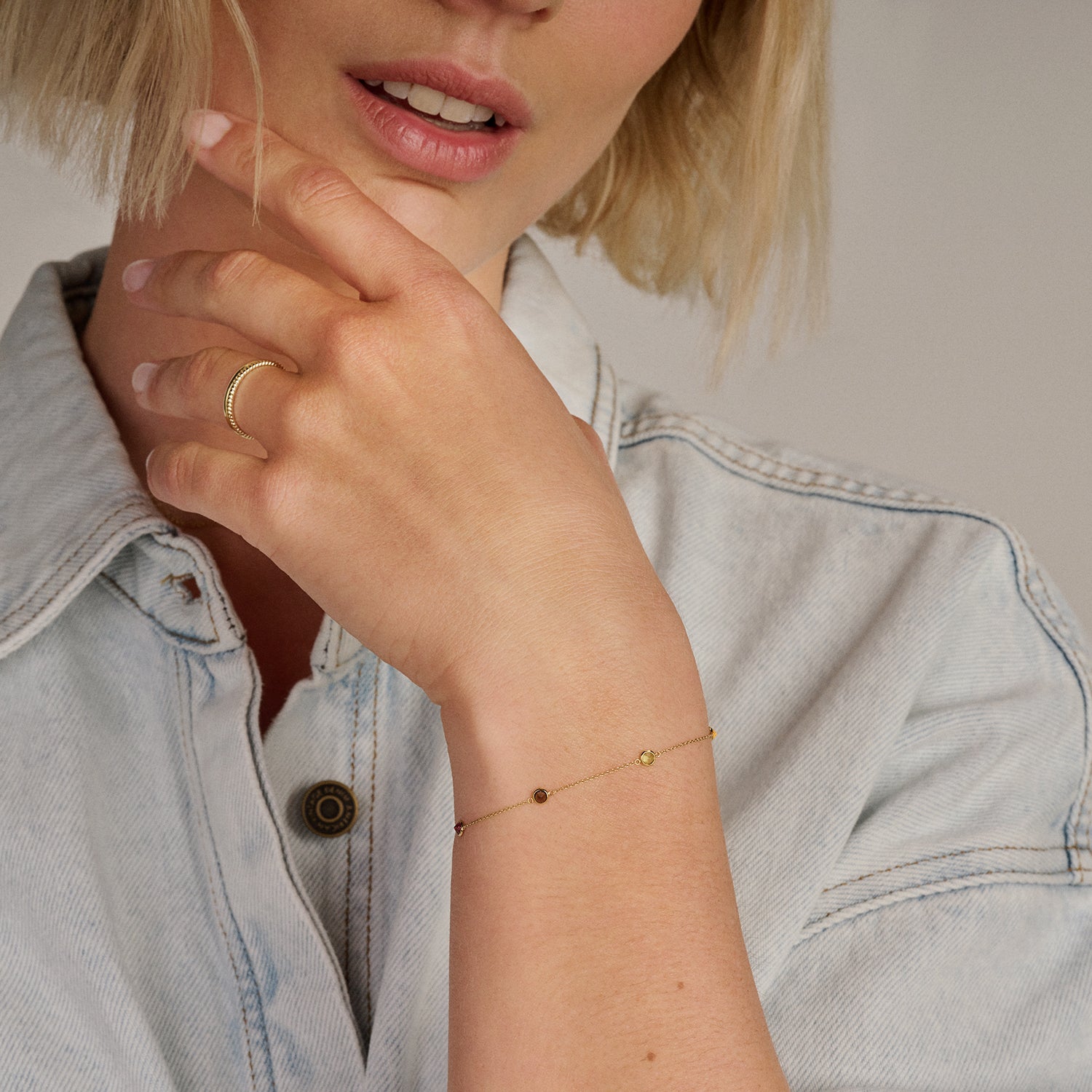 Fijne 14k goud armband met kleine gekleurde stenen aan slanke pols.