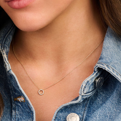 Fijne ketting met ronde zirkonia pavé hanger in 14k goud, gedragen bij jeansjas.