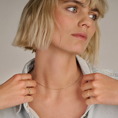 Fijne 14k goud ketting met subtiele schakelstructuur, gedragen door vrouw.