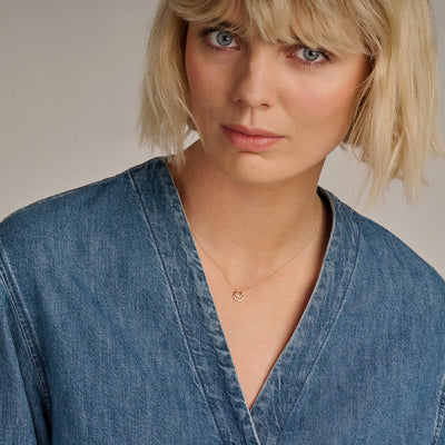 Fijne ketting van 14k goud met kleine zirkonia hanger gedragen bij een spijkerblouse.