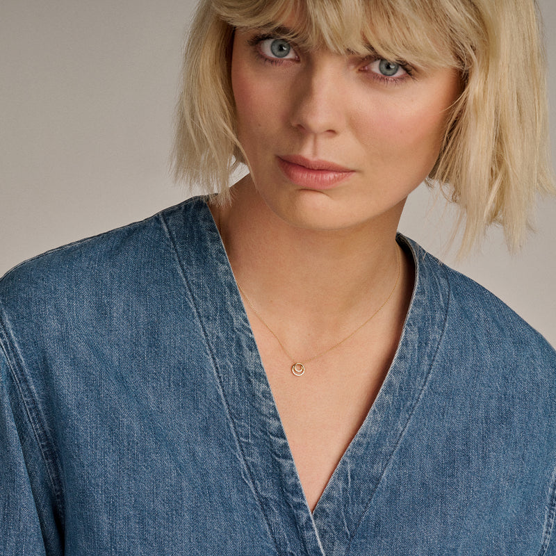 Fijne ketting van 14k goud met kleine zirkonia hanger gedragen bij een spijkerblouse.