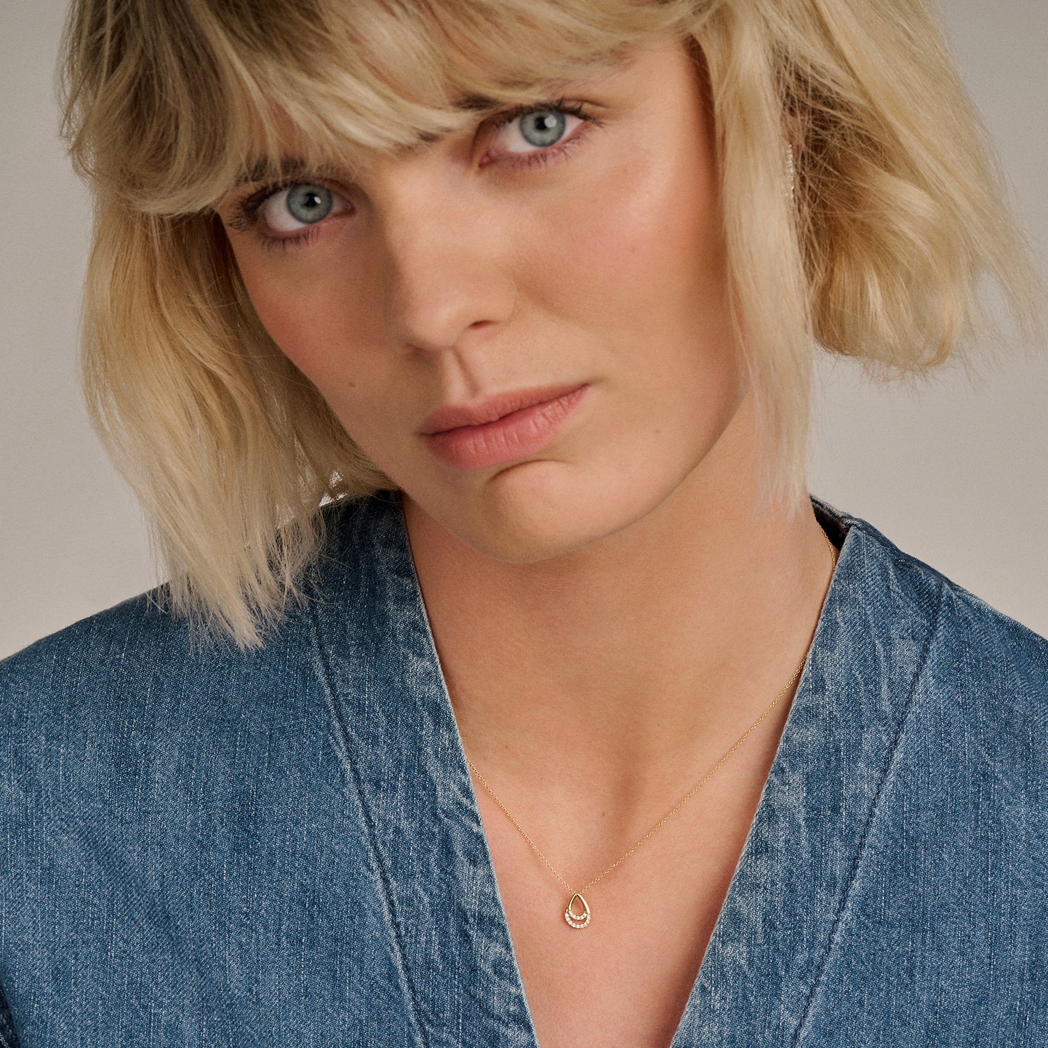 14k goud ketting met fijne schakels en zirkonia hanger gedragen bij een denim blouse.