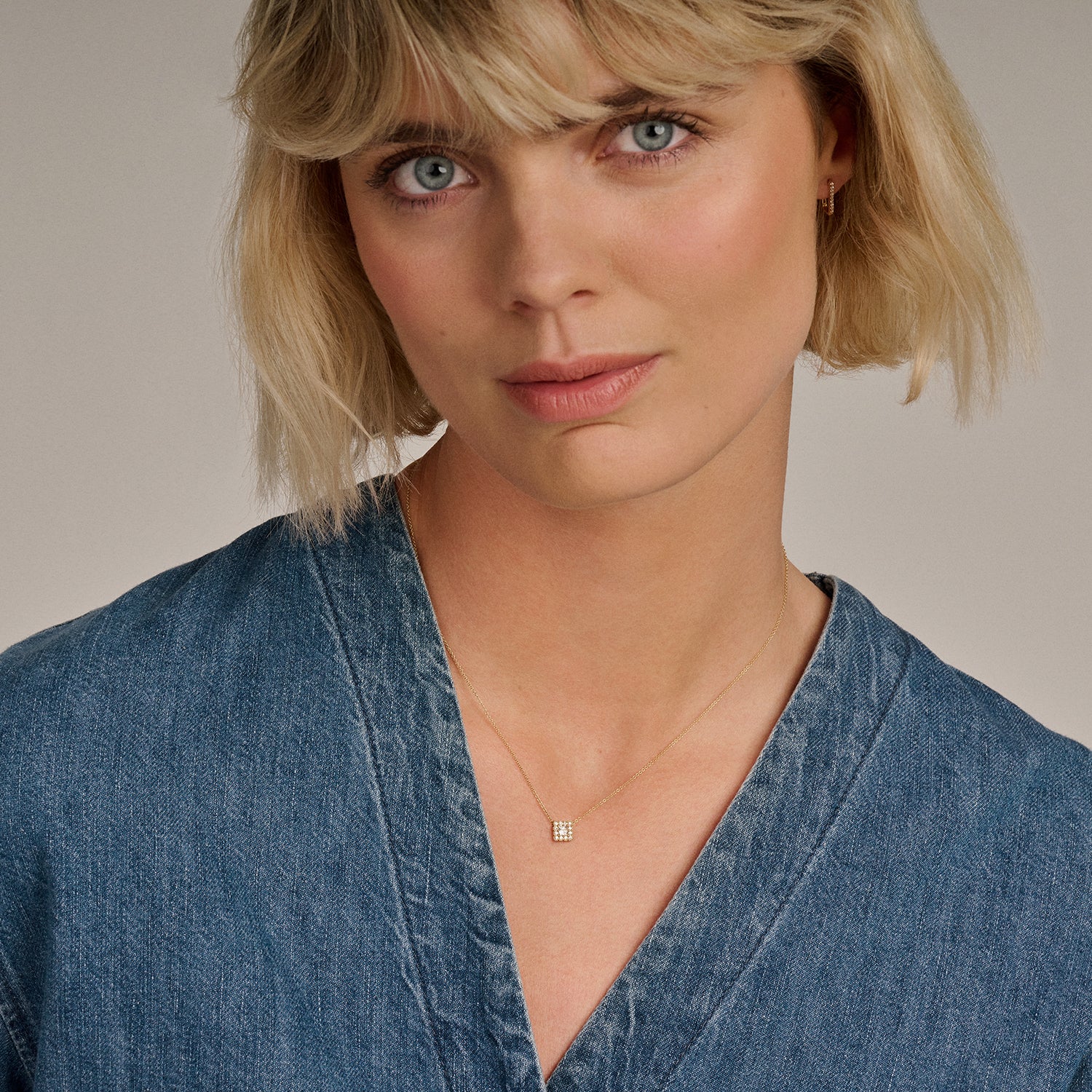 Fijne ketting van 14k goud met kleine zirkonia hanger gedragen door vrouw in denim blouse.