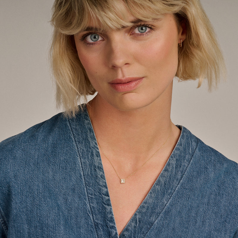 Fijne ketting van 14k goud met kleine zirkonia hanger gedragen door vrouw in denim blouse.