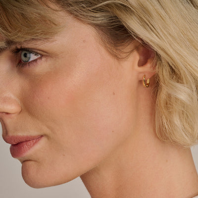 Kleine oorringen van 14k goud met gladde, ronde vorm gedragen door vrouw.