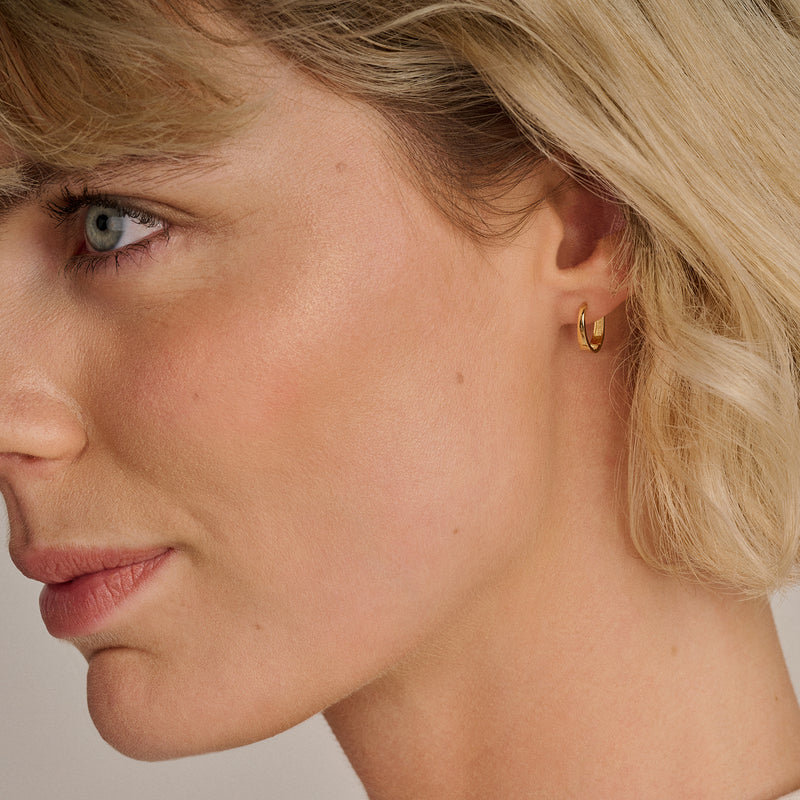 Kleine oorringen van 14k goud met gladde, ronde vorm gedragen door vrouw.