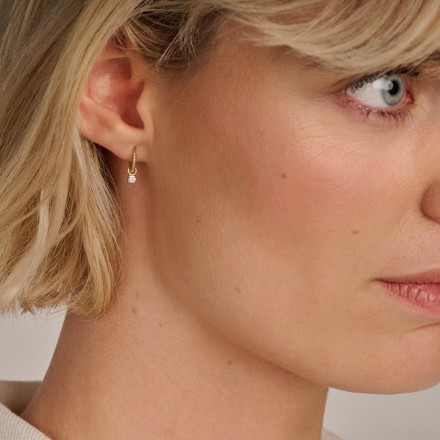 14k goud oorbellen met kleine hanger en zirkonia aan oor van vrouw.